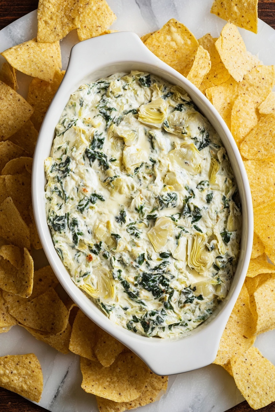 A close-up view of a white ceramic dish filled with creamy spinach and artichoke dip, showing a woman's hand holding a triangular yellow tortilla chip dipped into the dip. The dip has a thick, melted cheese texture with visible green spinach leaves and pale yellow artichoke pieces mixed throughout. Thin strands of melted cheese stretch from the dish to the chip, highlighting its gooey texture. The dish sits on a white marbled surface. Photo taken with an iphone --ar 2:3 --v 7
