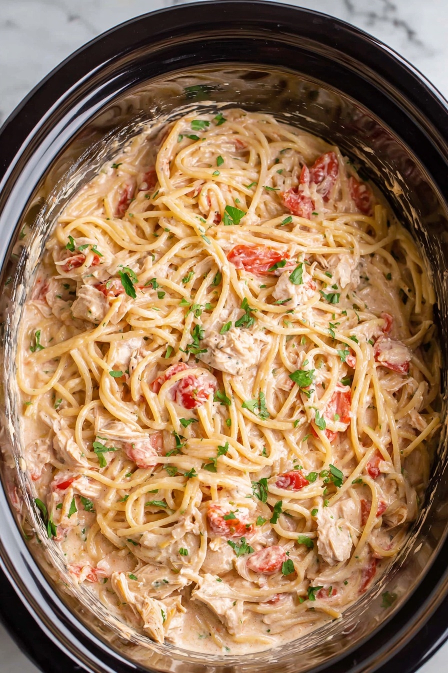 The image shows a slow cooker filled with creamy spaghetti. The spaghetti is mixed with small pieces of white chicken and chunks of red tomatoes, all covered in a light pink creamy sauce. The noodles are spread evenly in the slow cooker, with bits of chopped green herbs sprinkled on top. The inside of the cooker is shiny and dark, contrasting with the creamy pasta. The background is a white marbled texture. photo taken with an iphone --ar 2:3 --v 7
