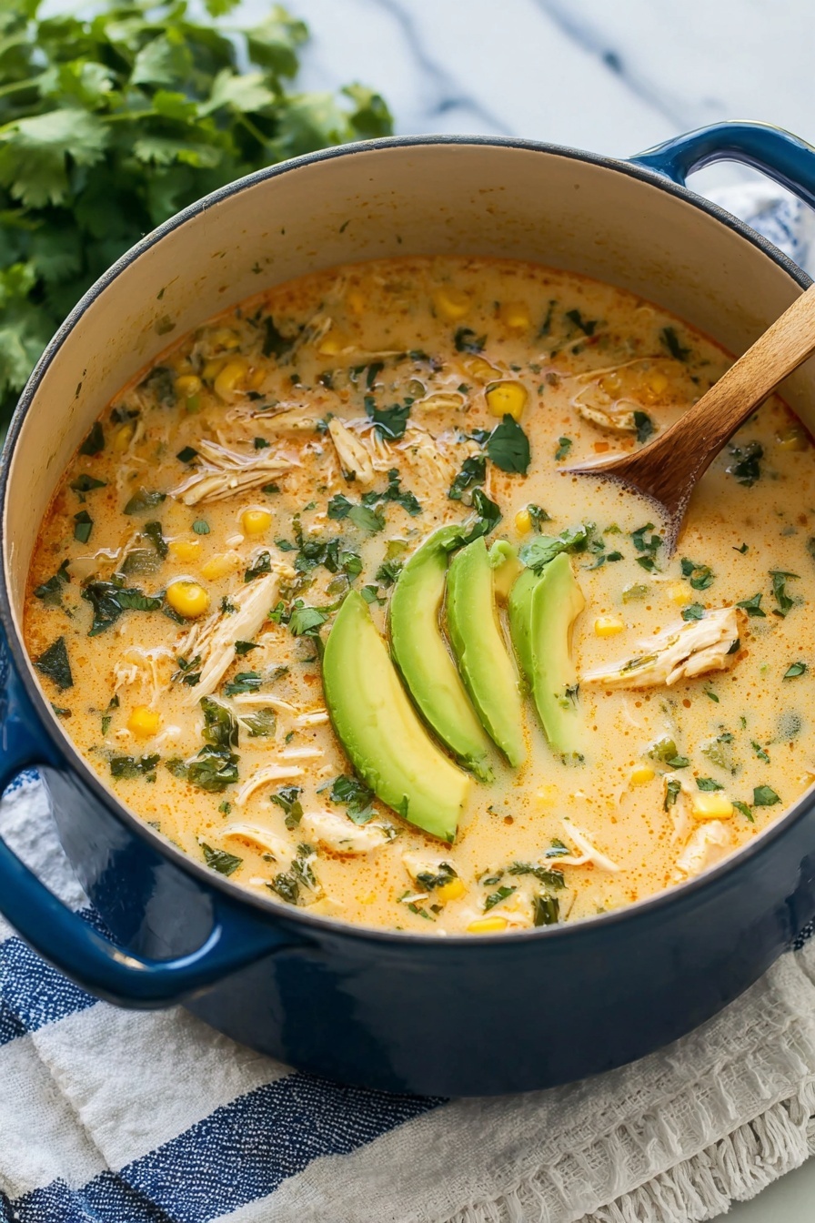The image shows a white bowl filled with creamy light beige soup that has visible pieces of white beans, yellow corn, shredded white meat, and green herbs mixed in. On top of the soup, there are three yellowish triangular tortilla chips placed in a row on the left side, a fan of bright green avocado slices next to them, a wedge of green lime in the middle, and a small pile of white shredded cheese in the center. The bowl sits on a white plate, and a silver spoon is placed on the right side of the plate. The setting includes a white marbled surface with some green cilantro leaves and a halved avocado nearby. Photo taken with an iphone --ar 2:3 --v 7
