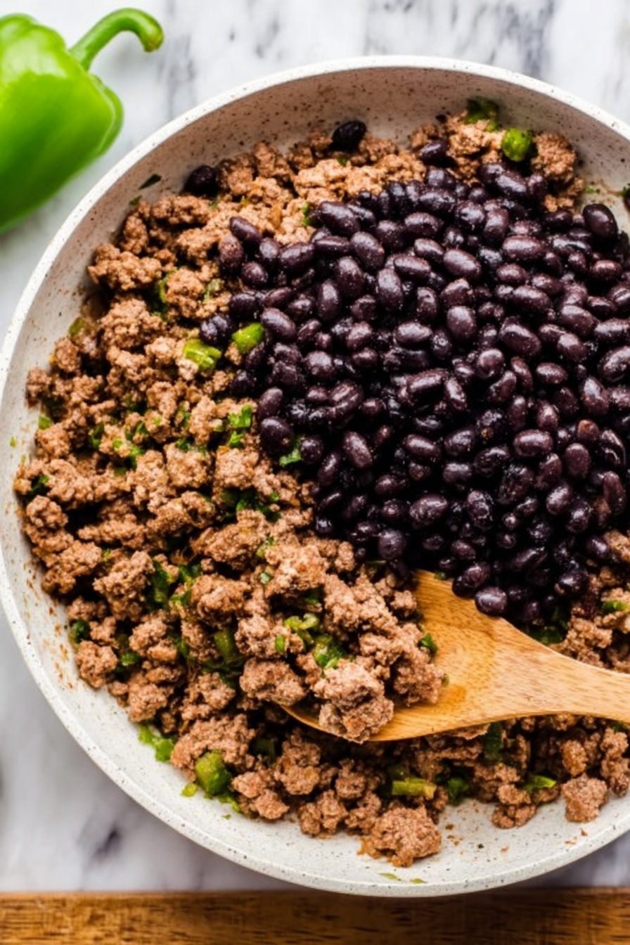 A white round plate holds a layer of yellow corn tortilla chips spread out in a circle. On top, there is a layer of cooked brown ground meat and melted orange cheese, scattered with dark sliced black olives. Next, bright green jalapeño slices, cherry tomato halves, and fresh green cilantro leaves are spread evenly. In the center, there is a dollop of white sour cream sprinkled lightly with red paprika. The plate rests on a wooden surface next to a white bowl of red salsa, completing the scene. photo taken with an iphone --ar 2:3 --v 7