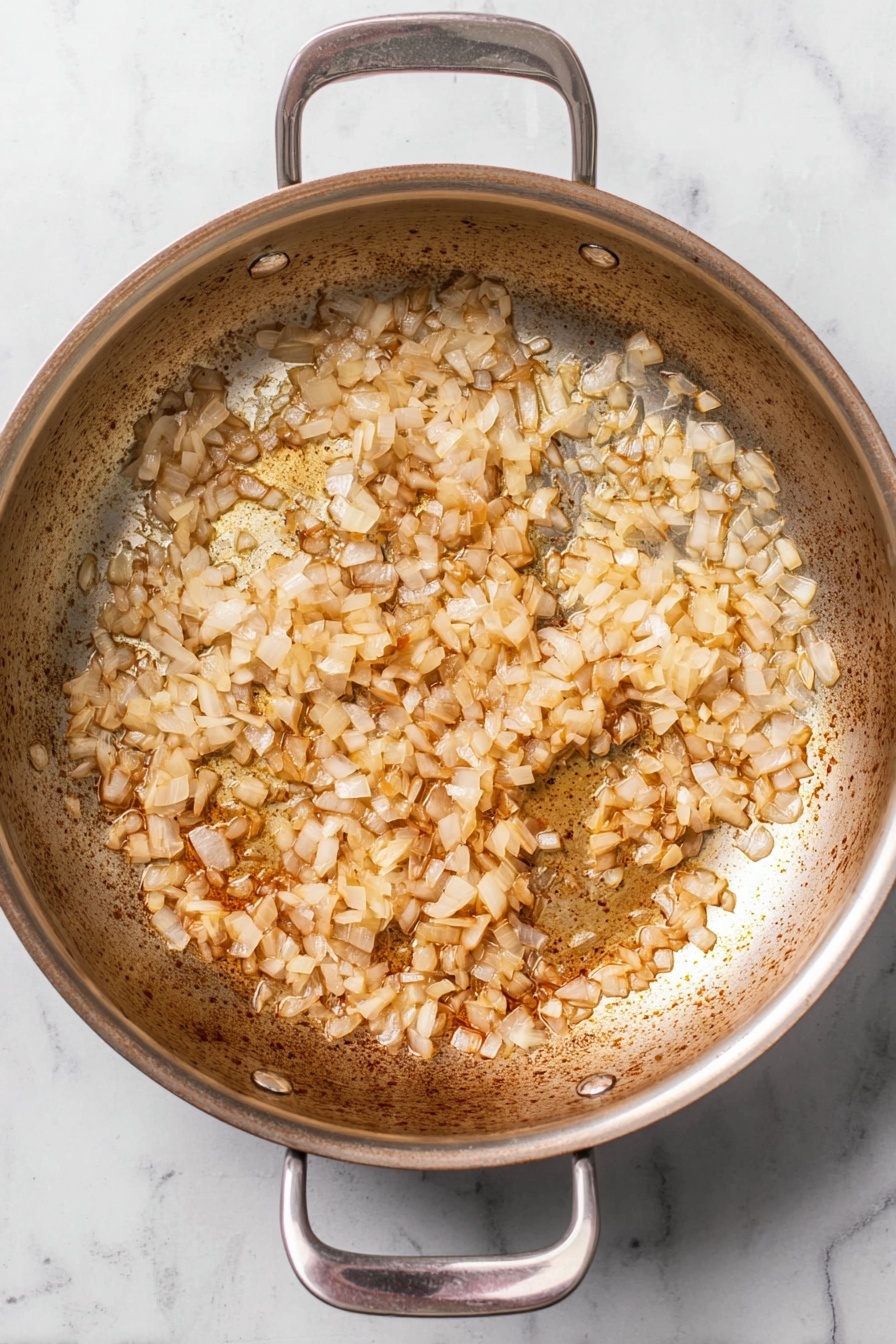A round stainless steel pan with two handles shows a single layer of small, diced onions cooked to a light brown color, spread evenly inside the pan. The pan’s interior surface has some browned spots and slight char marks. The pan rests on a white marbled surface photo taken with an iphone --ar 2:3 --v 7